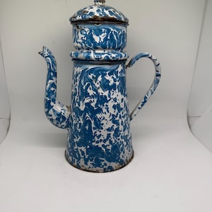 May include: Vintage blue and white enamelware coffee pot with a lid. The pot features a unique marbled pattern in shades of blue and white. It has a spout, handle, and a separate top section, typical of a coffee percolator. The pot is approximately 10 inches tall.