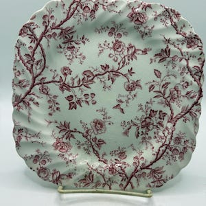 May include: A square ceramic plate with a scalloped edge, featuring a white base and a detailed maroon floral pattern of branches and blossoms. The surface has a visible crackle glaze finish throughout the entire design of the plate.
