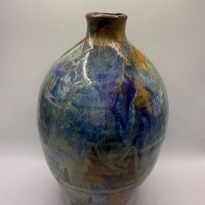 May include: A handcrafted ceramic vase with a wide, rounded body and a narrow neck. The vase features a blend of blue, green, and brown glaze, creating a marbled effect. The vase is approximately 12 inches tall.