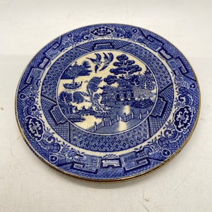 Puede incluir: Un pequeño plato de porcelana azul y blanco con un borde dorado. El plato presenta un tradicional patrón de sauce con una pagoda, un puente, un sauce llorón y pájaros.