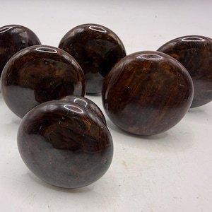 May include: A set of six round cabinet knobs featuring a polished, dark brown marbled finish with swirling patterns of deep mahogany and black tones. Each knob has a smooth, glossy surface and a rounded, dome-shaped profile for furniture hardware.
