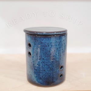 May include: A cylindrical ceramic container with a lid, glazed in a deep blue with a speckled texture. The container has several small, evenly spaced holes and the text "READY TO SHIP" is arched above the container.