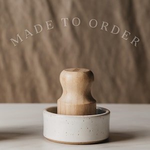 May include: A light-colored wooden muddler with a rounded top is set in a small, speckled white ceramic bowl. The text "MADE TO ORDER" is arched above the muddler. The background is a neutral brown.