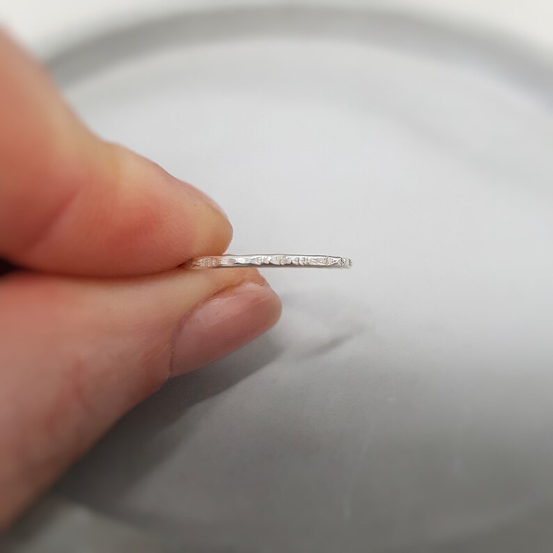 May include: A thin silver band ring with a textured surface.