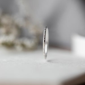 May include: A thin silver band ring with a textured edge.