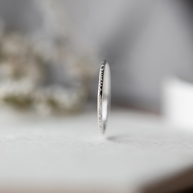 May include: A thin silver band ring with a textured edge.