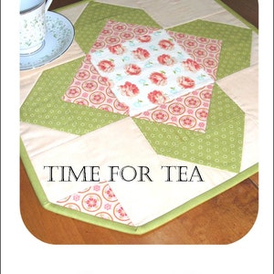 Pode incluir: Um corredor de mesa acolchoado verde, branco e rosa com um design geométrico. O corredor tem uma borda verde e o texto "TIME FOR TEA" em letras pretas.