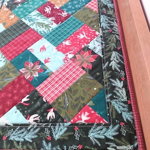 May include: A green, red, and blue patchwork table runner with a Christmas theme. The runner has a green border with a white holly pattern and a red border with a white dot pattern.