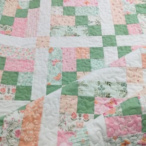 May include: A patchwork quilt featuring a mix of floral, butterfly, and solid fabric squares in shades of pink, green, peach, and white. The quilt has a quilted pattern throughout.