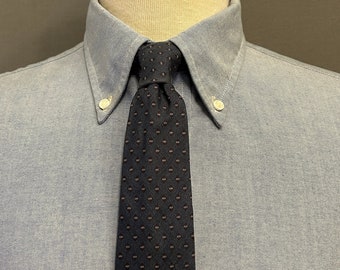 Peut inclure: Une chemise boutonnée bleu clair avec une cravate bleu marine ornée de petits pois rose-rouge. La chemise a un col classique et des boutons. La cravate est nouée et centrée.