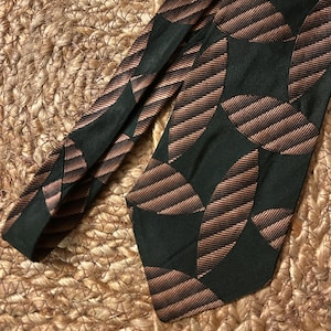 May include: A black and brown patterned tie with a geometric design. The tie has a repeating pattern of circles with stripes.