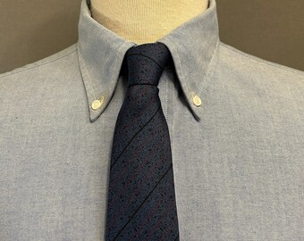 May include: A light blue button-down shirt with a dark blue and red striped tie. The tie has a subtle pattern of small red dots.