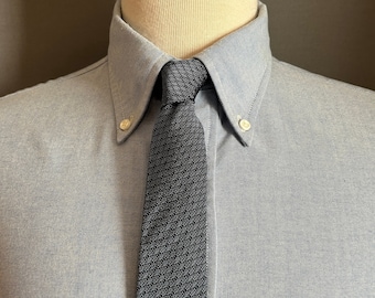 Peut inclure: Une chemise boutonnée bleu clair avec une cravate tricotée gris foncé. La cravate est nouée et centrée, avec un motif texturé. La chemise a un col boutonné et de petits boutons blancs.