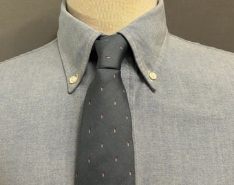 May include: A light blue button-down shirt with a dark blue tie featuring a white and red pattern. The tie has a small, thin white stripe near the top.