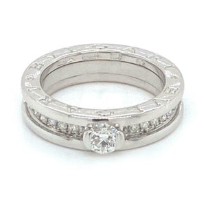 May include: A silver ring with a single diamond set in the center and a row of smaller diamonds around the band. The ring has an engraved design on the band.