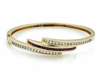 Puede incluir: Un brazalete de oro con un diseño curvo que presenta una fila de piedras preciosas rojas y una fila de piedras preciosas transparentes.