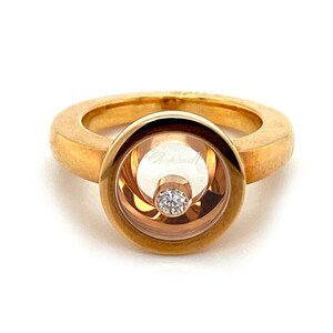 May include: A gold ring with a round, clear, floating diamond in the center. The ring has a Chopard inscription on the inside of the band.