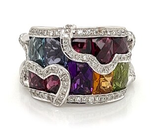 May include: A white gold ring with a multi-colored gemstone design. The ring features a heart shape with a variety of gemstones, including amethyst, aquamarine, citrine, peridot, and ruby.