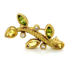 May include: A gold brooch with a textured stem and four leaves set with green and yellow gemstones. The brooch is accented with small diamonds.
