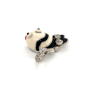 May include: A white and black enamel fish charm with red accents and a diamond-encrusted bail. The fish has a black bow on its tail.