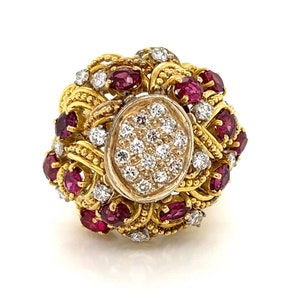 May include: A gold ring featuring an oval cluster of small diamonds at the center, surrounded by a halo of oval-cut rubies and smaller diamonds. The ring has a textured gold band and intricate detailing.