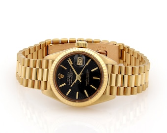 May include: A gold Rolex Oyster Perpetual Datejust wristwatch with a black face and a gold band. The watch has a date window at the 3 o'clock position and the text "Rolex Oyster Perpetual Datejust" is printed on the face.