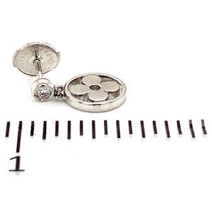 K&ouml;nnte beinhalten: Ein silberner Ohrring mit einem bl&uuml;tenf&ouml;rmigen Anh&auml;nger und einem kleinen Diamanten. Der Ohrring ist etwa 2,5 cm lang.