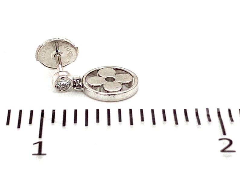 K&ouml;nnte beinhalten: Ein silberner Ohrring mit einem bl&uuml;tenf&ouml;rmigen Anh&auml;nger und einem kleinen Diamanten. Der Ohrring ist etwa 2,5 cm lang.