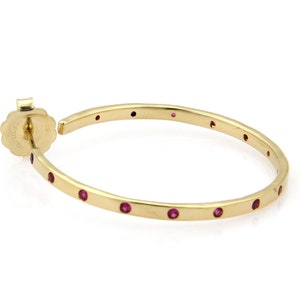 Op de afbeelding: Gouden creolen met kleine rode edelstenen rondom de rand.