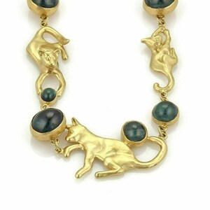 May include: A gold necklace with green gemstone beads and cat charms. The necklace is made of 14k gold and features a unique design with cats playing with balls of yarn.