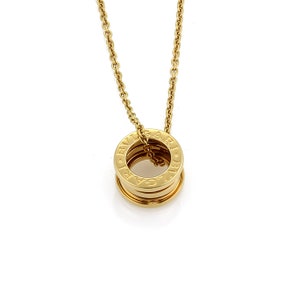 May include: A gold necklace with a pendant featuring multiple stacked rings with the inscription "BVLGARI" around each ring.