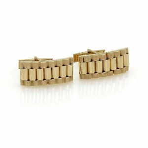 May include: A pair of gold-colored cufflinks. Each cufflink features a rectangular design with a series of vertical, cylindrical links, resembling a watch band. The cufflinks have a polished finish and a classic, elegant style.