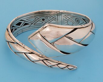 May include: A silver, braided, snake-shaped bangle bracelet. The bracelet is open and has a hinged clasp.