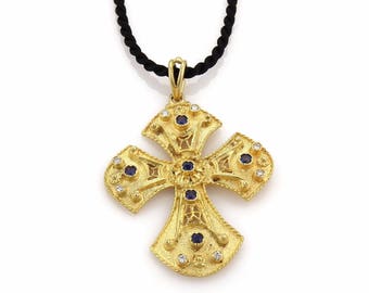May include: A gold cross pendant with blue and white gemstones. The pendant is on a black cord necklace.