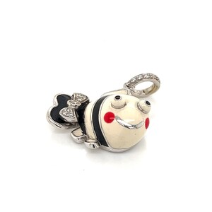 May include: A white and black enamel fish charm with red cheeks and a diamond bow. The charm has a silver loop for attaching to a bracelet or necklace.
