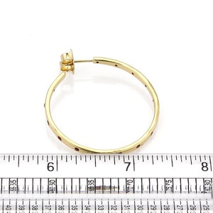 Op de afbeelding: Gouden creolen met rode edelstenen die in de band zijn gezet. De oorbellen hebben een diameter van ongeveer 5 cm.