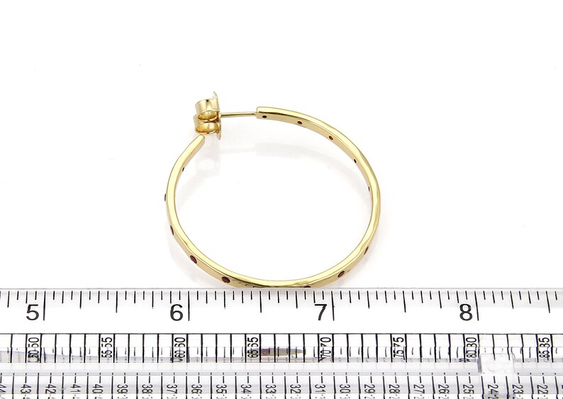 Op de afbeelding: Gouden creolen met rode edelstenen die in de band zijn gezet. De oorbellen hebben een diameter van ongeveer 5 cm.