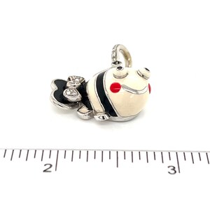 May include: A white and black enamel fish charm with red accents and diamond accents on the tail. The charm is made of silver and is about 1 inch long.