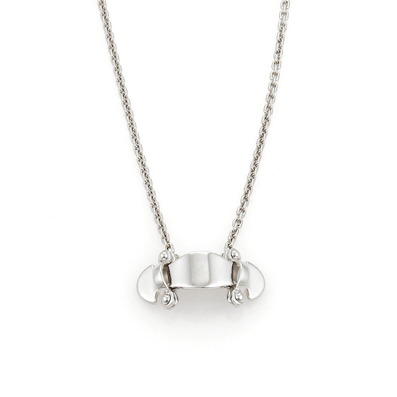 Puede incluir: Un collar de cadena de plata con un colgante &uacute;nico que presenta un dise&ntilde;o curvo abierto con dos peque&ntilde;os acentos redondos a cada lado.