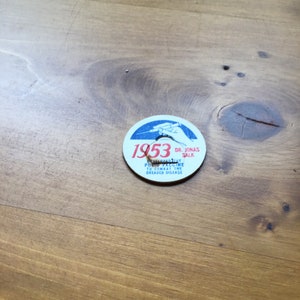 May include: A white round button with blue and red lettering. The button commemorates the 1953 polio vaccine developed by Dr. Jonas Salk. The text reads "1953, Dr. Jonas Salk, Polio Vaccine to Combat the Dreaded Disease."