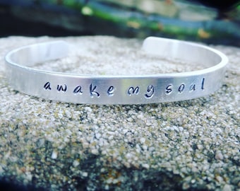 Brazalete de aluminio estampado a mano de Mumford & Sons con la letra "despierta mi alma".