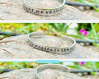 Pulsera de aluminio estampada a mano con la letra "Ilumíname, estoy perdido en la oscuridad" y alas inspiradas en Mumford and Sons.