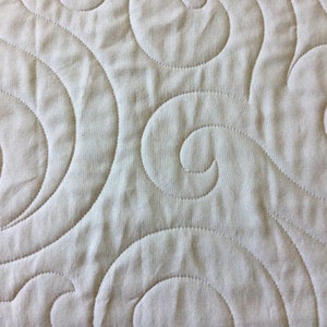 May include: A close-up of a beige fabric with a quilted pattern of swirling lines.