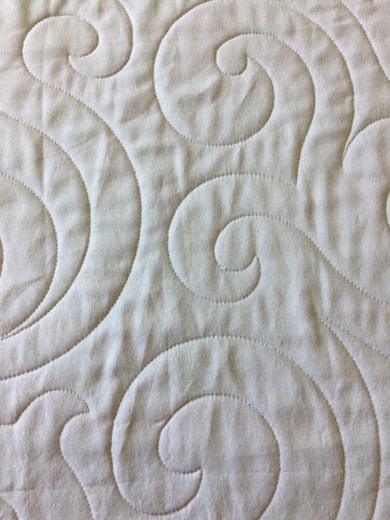 May include: A close-up of a beige fabric with a quilted pattern of swirling lines.