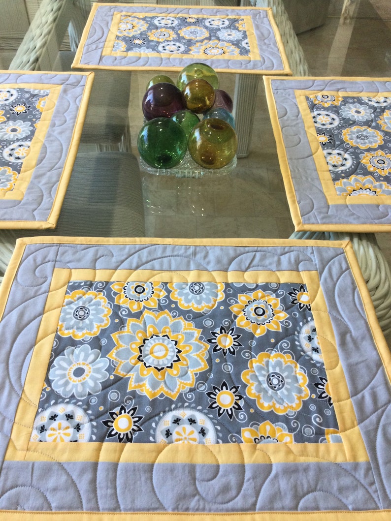 May include: Set of four gray and yellow quilted placemats with a floral pattern. The placemats have a scalloped edge and a yellow border.