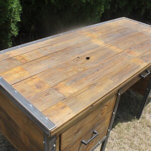 May include: A rustic wooden desk with metal accents and two drawers. The desk has a distressed wood finish and a metal frame.