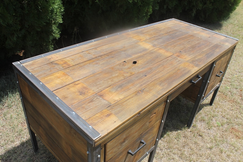 May include: A rustic wooden desk with metal accents and two drawers. The desk has a distressed wood finish and a metal frame.