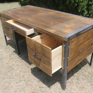 May include: A rustic wooden desk with metal accents and three drawers. Two drawers are open, revealing the wood interior. The desk is made of reclaimed wood and has a distressed finish.