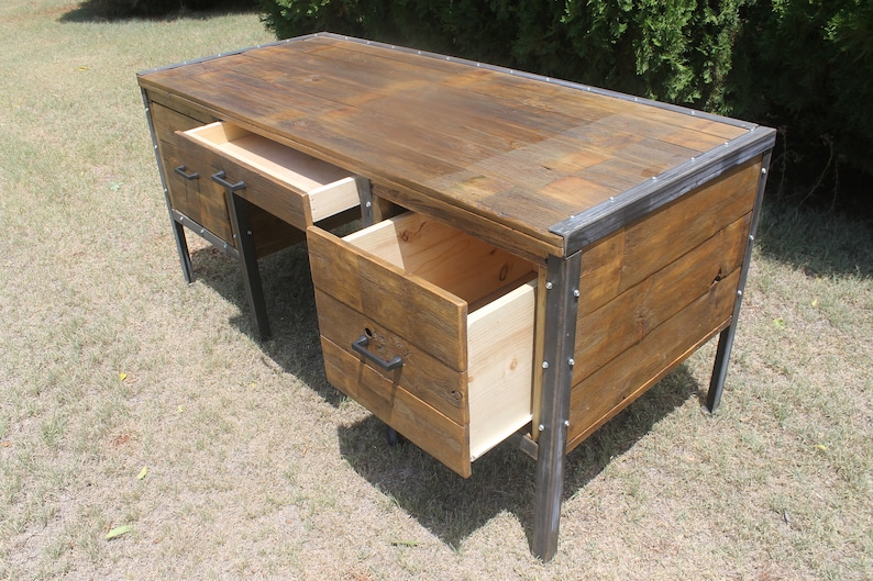 May include: A rustic wooden desk with metal accents and three drawers. Two drawers are open, revealing the wood interior. The desk is made of reclaimed wood and has a distressed finish.