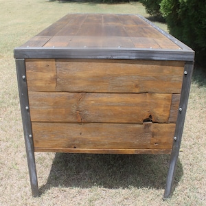 May include: A rustic wooden desk with a metal frame and legs. The desk has a natural wood finish and is made of reclaimed wood. The metal frame is painted a dark gray color.